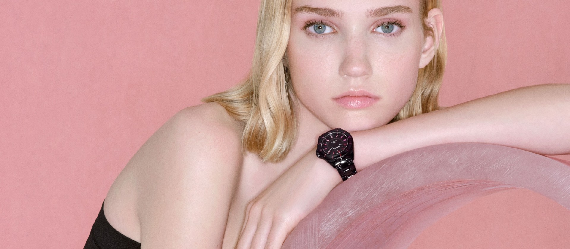 Model wearing a black luxury watch against a pink setting
